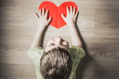 Child placing hands on a red paper heart on the floor.