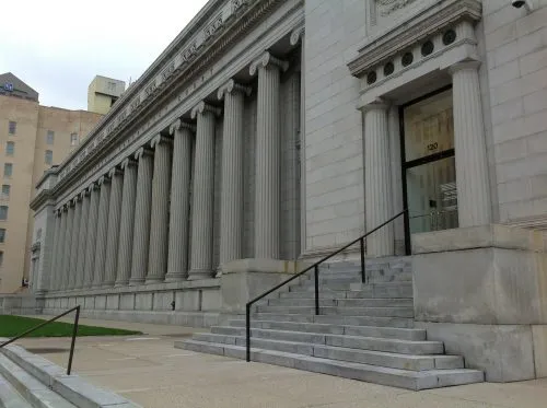 Row of classical columns on a large stone building with steps leading to an entrance.