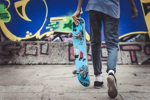 Person holding a skateboard walks past a colorful graffiti-covered wall.