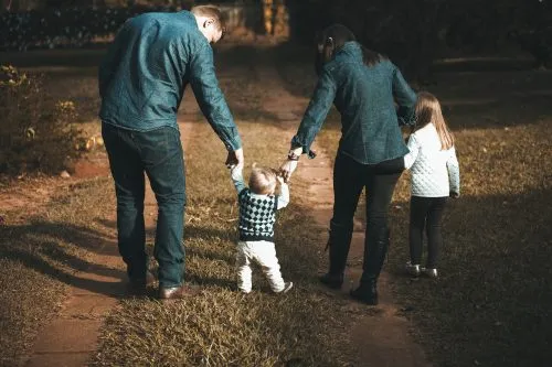 A family walks outside, holding hands with a toddler between them.
