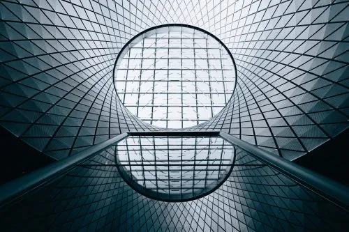 View of a geometric ceiling with a circular skylight and reflective surfaces.