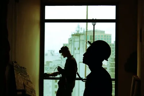 Silhouetted construction workers in front of a cityscape through a large window.