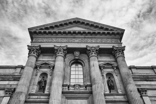 Historic building facade with tall columns and detailed sculptures under a cloudy sky.