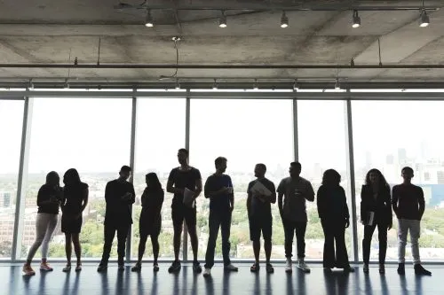 Silhouetted group of people standing in front of large windows with a city view.