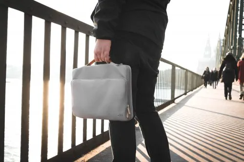 Person holding a gray bag while walking on a sunlit bridge walkway.