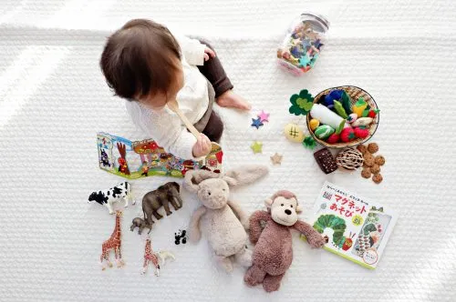 Baby playing with toys and books on a white blanket.