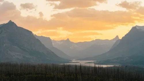 Mountain valley at sunset with a river and silhouetted peaks.