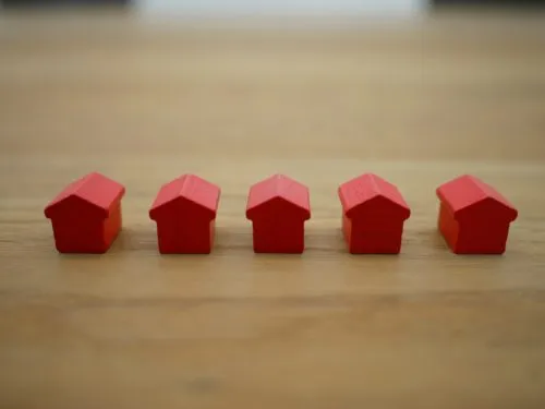 Five small red toy houses aligned on a wooden surface.