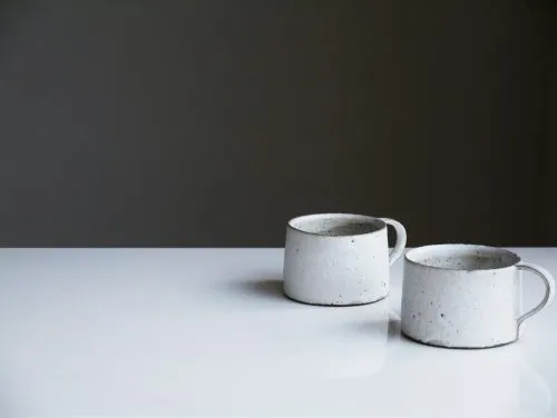 Two white ceramic mugs on a reflective white surface against a dark background.