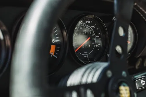 Close-up of a vintage car speedometer and steering wheel.