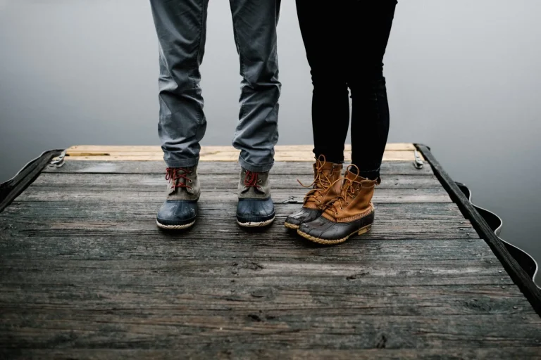 Two people wearing boots stand side by side on a wooden dock.