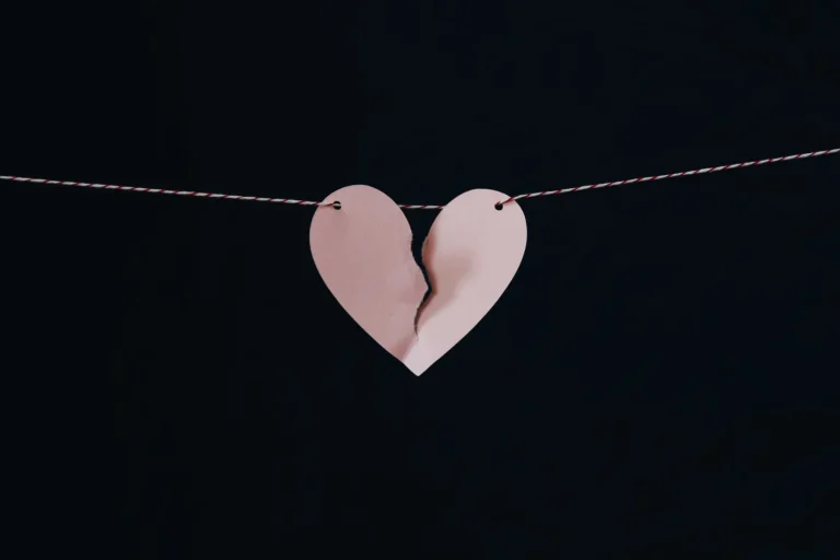 A torn pink paper heart hanging on a string against a dark background.